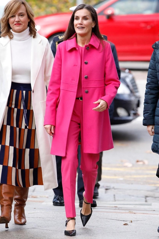 Kraljevo fluorescentno rožnato obleko sestavlja plašč do kolen, rahlo razvlečen, s kontrastnimi črnimi gumbi, ki se ujemajo s čevlji s …